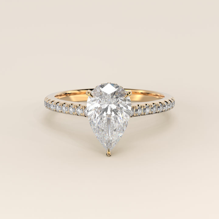Bague de fiançailles en or jaune, sertie d'un diamant de laboratoire taille poire, avec pavage et halo discret sur l'anneau pavé.
