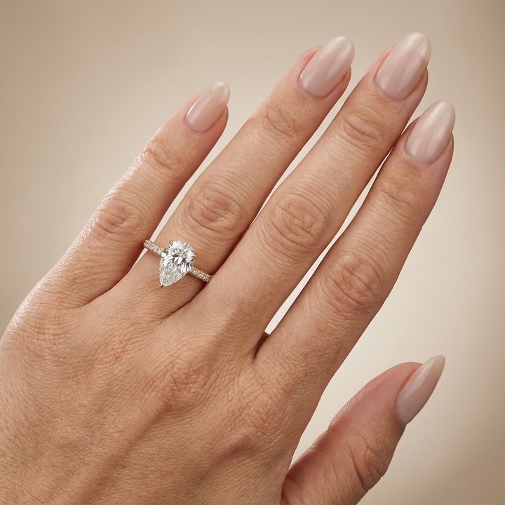 Bague de fiançailles en or jaune, sertie d'un diamant de laboratoire taille poire, avec pavage et halo discret sur l'anneau pavé.