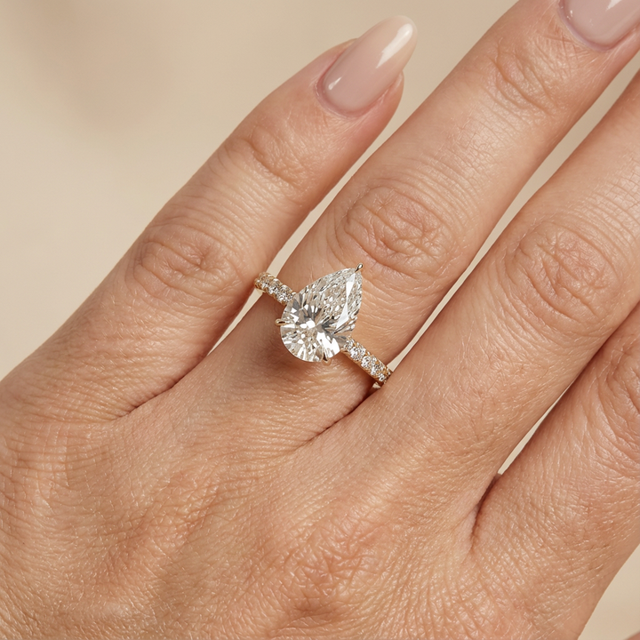 Bague de fiançailles en or jaune, sertie d'un diamant poire de laboratoire avec halo discret et pavage sur l'anneau.